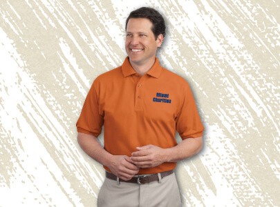 Man wearing orange, button down, cotton polo shirt with embroidered Miami Charities logo on chest. Wearing as a work uniform.