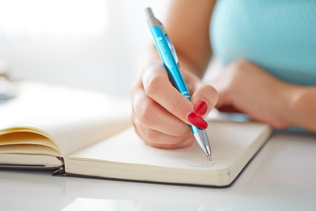 woman writing in a planner with a custom printed pen featuring Miami Savings logo